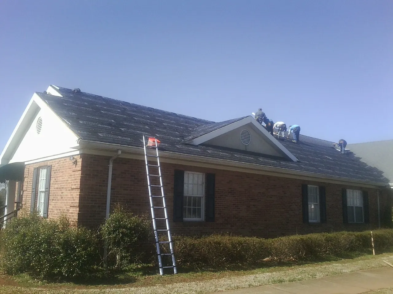 Crew tearing shingles off a brick ranch roof with a ladder set — Metal Roof Repair work by our crew in North Truro