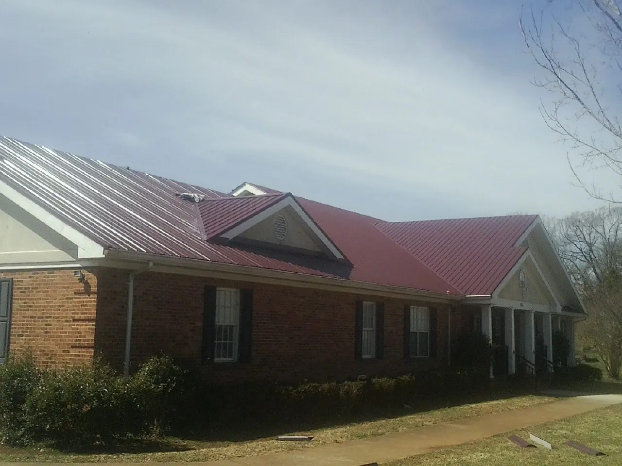 Red metal roof with gabled entries on a long brick building, from a Hail Damage Roof Repair job in North Truro