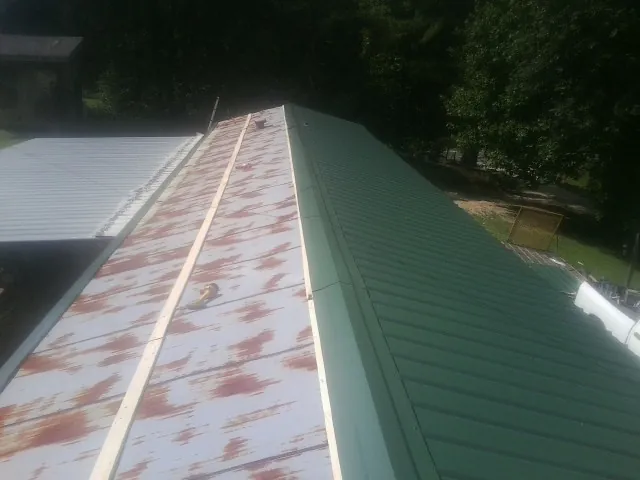 Old rusted panels beside newly installed green metal roofing — Wind Damage Roof Repair by Roofing Brothers in North Truro