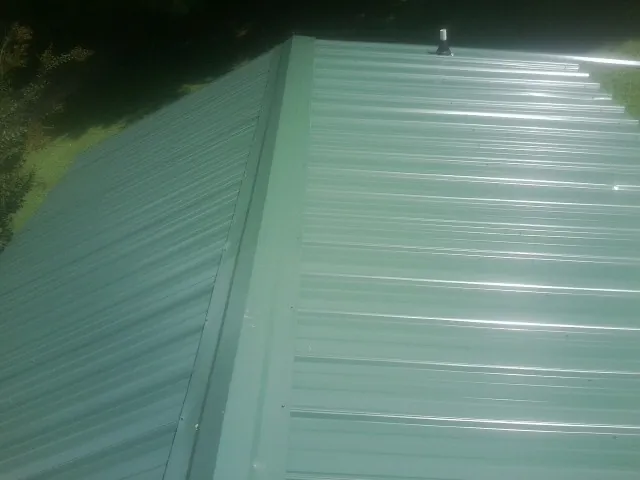 New green metal panels meeting at the ridge of a roof — Flat Roof Repair work by our crew in North Truro