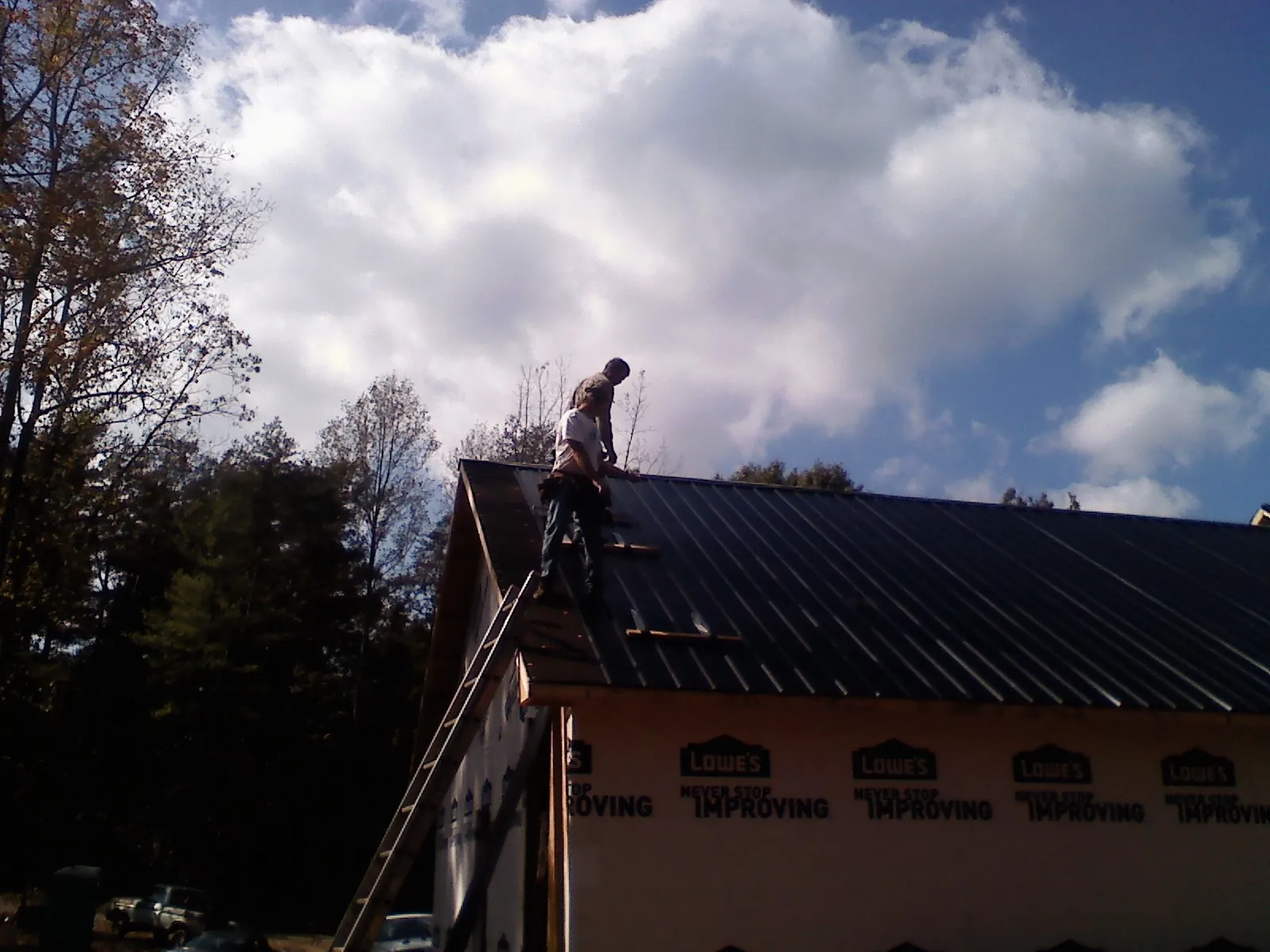 Roofer fastening dark metal panels high against a cloudy sky, from a Roof Inspection job in North Truro