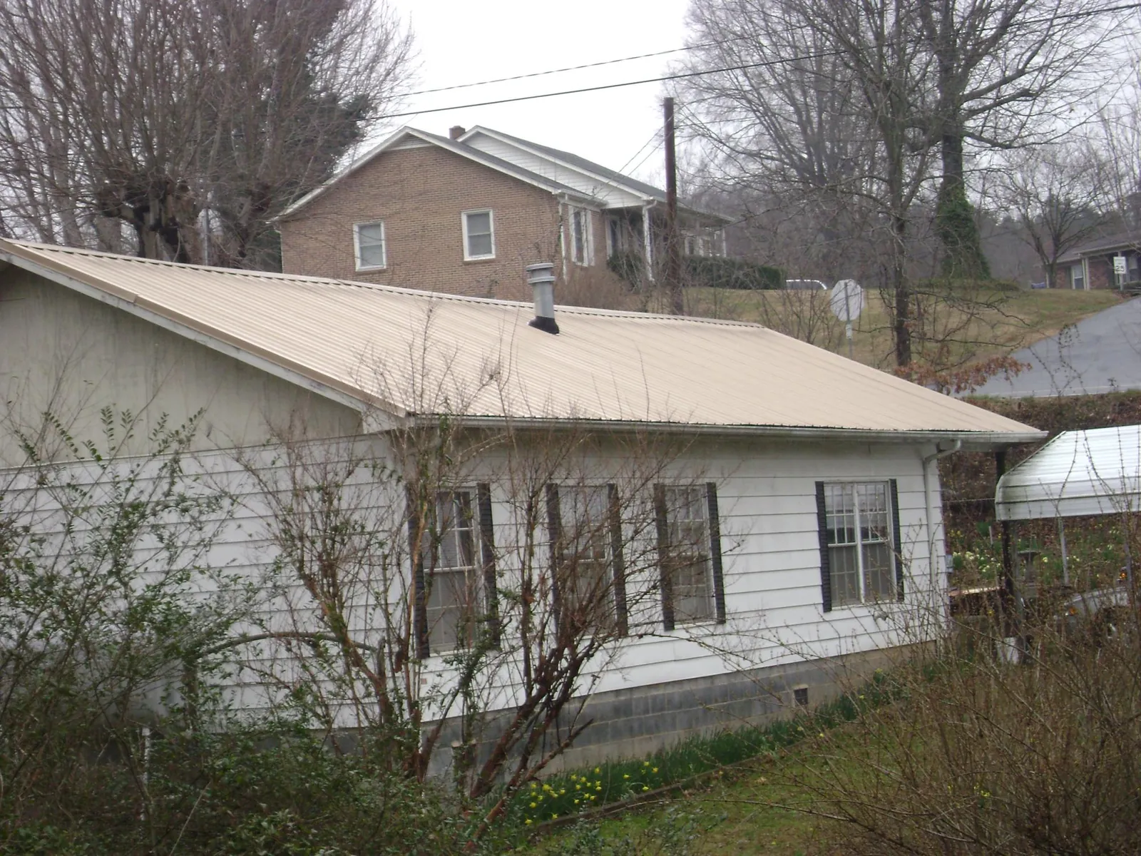 Tan metal roof on a white sided house set into a hillside — Commercial Roofing by Roofing Brothers in North Truro